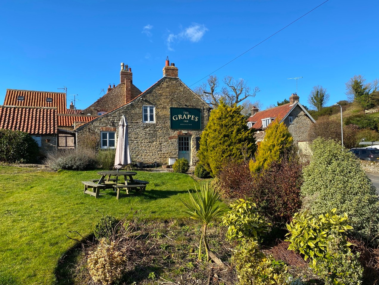 The Grapes Inn, a stone country pub with a lawned beer garden under a blue sky